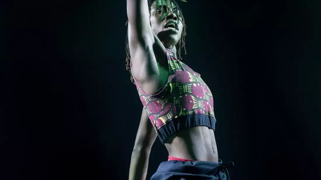 A photograph of a dancer stretching their right arm out of the top of the frame