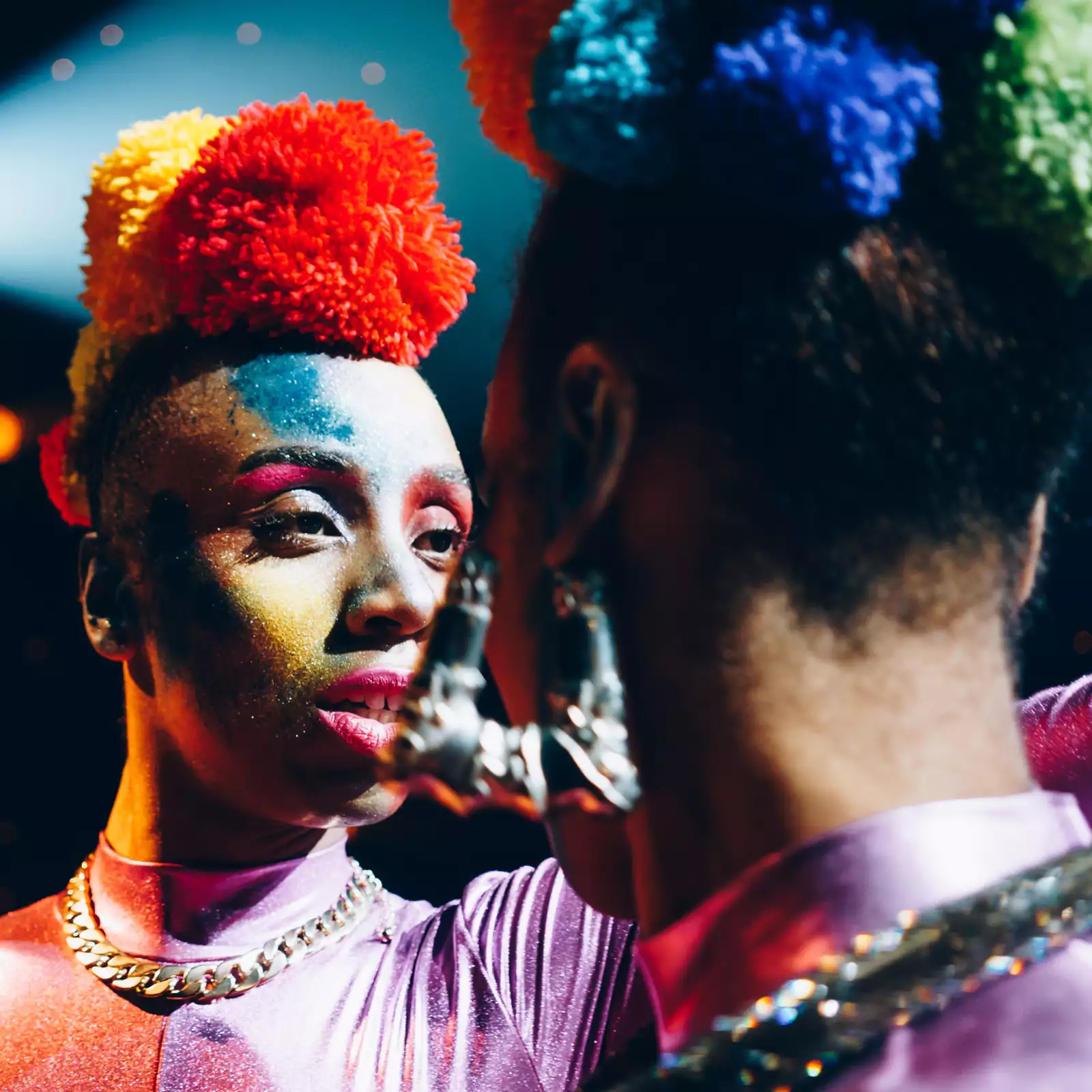 Two performers in brightly coloured outfits and make up face each other.
