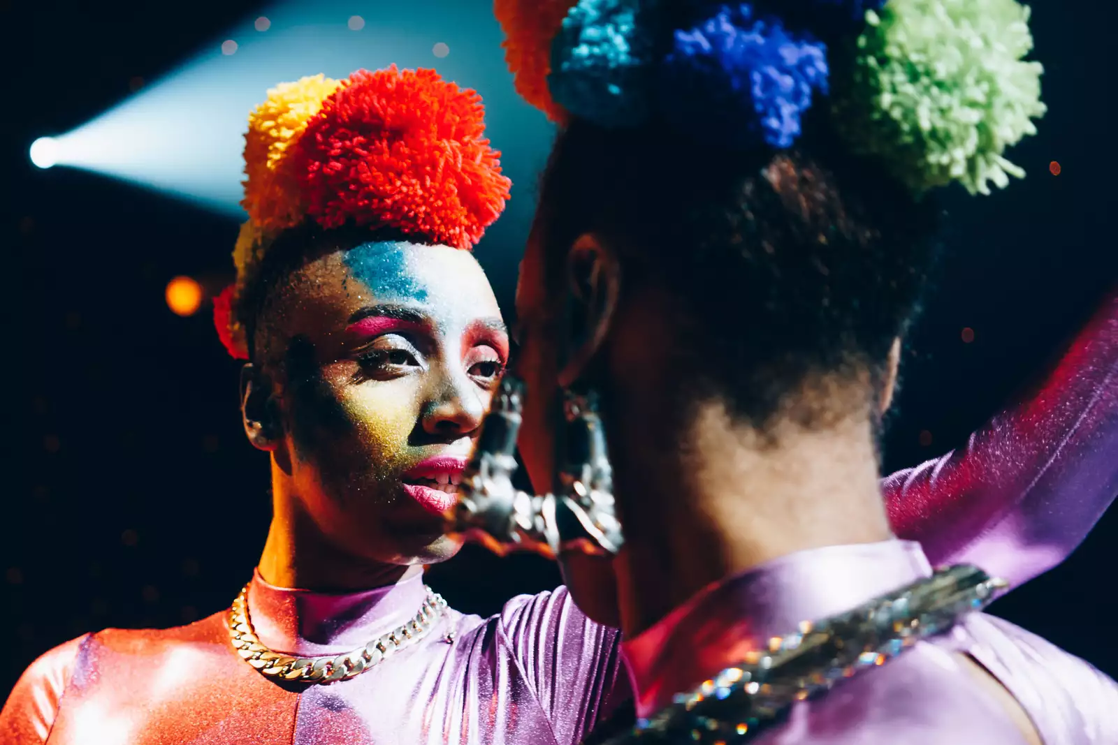 Two performers in brightly coloured outfits and make up face each other.