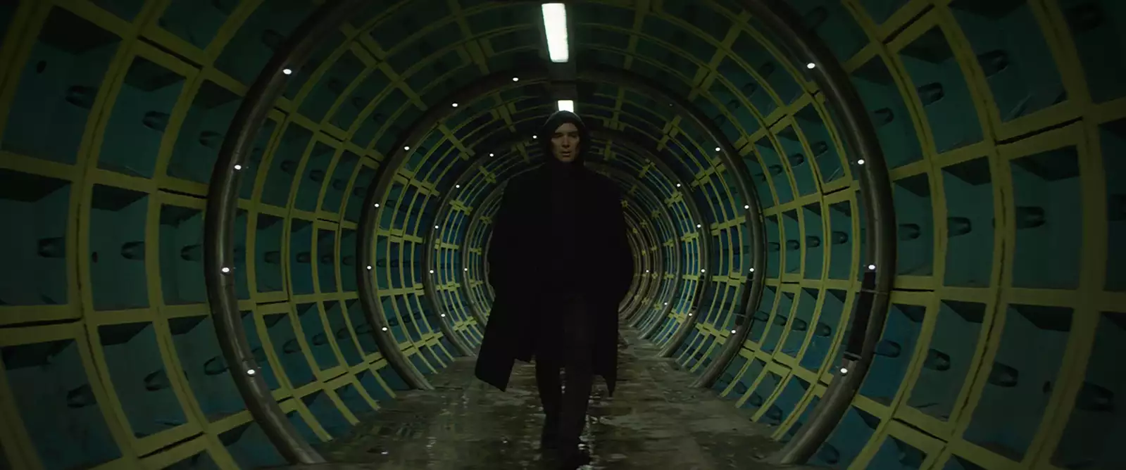 A still from All Of This Unreal Time, with Cillian Murphy walking towards the camera in a long, straight tunnel with green metal walls.