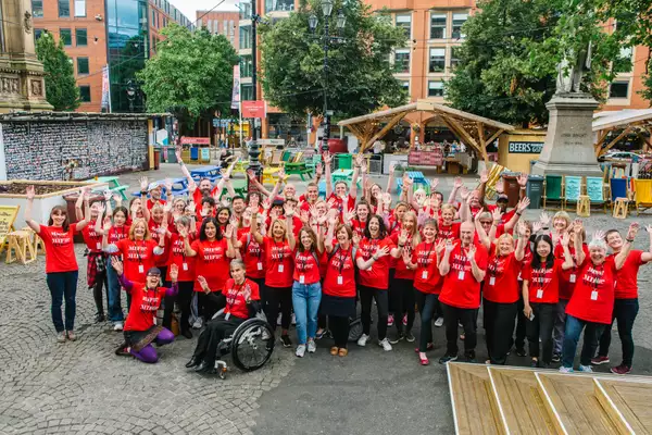 Group photo of MIF volunteers with outstretched arms in a town square