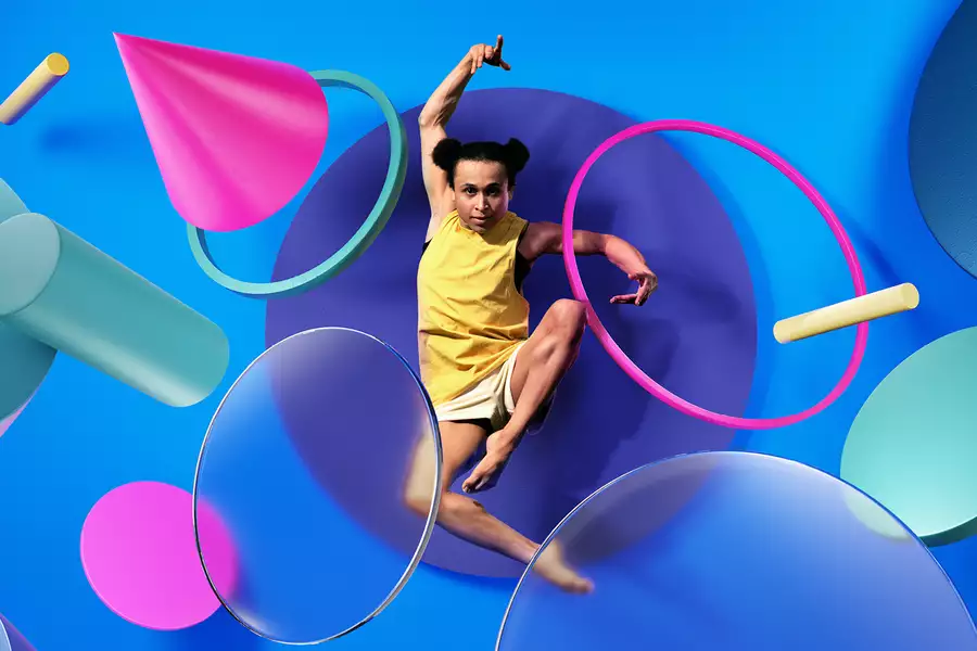 Performer leaping through and in front of colourful pink & turquoise rings and 3D shapes