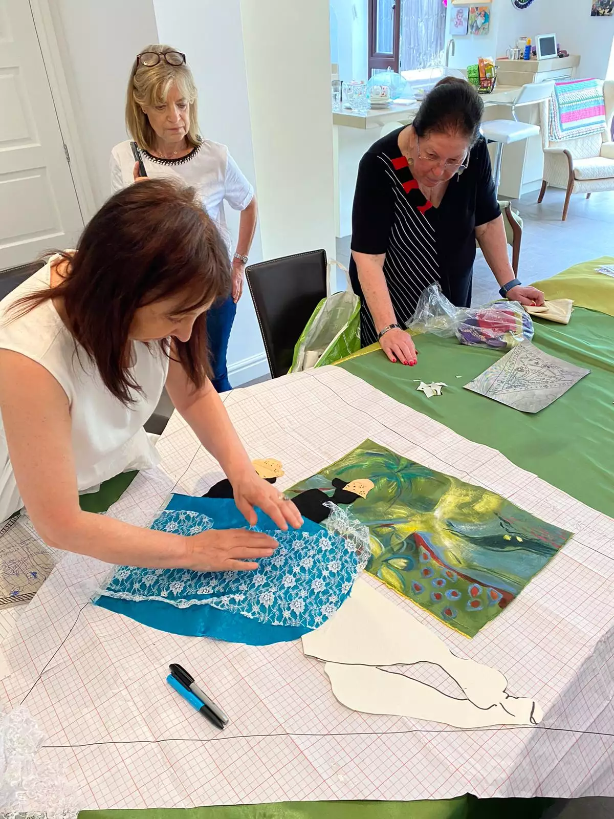 Three members of the Manchester Jewish Museum textiles group stand at a work table making fabric collage.